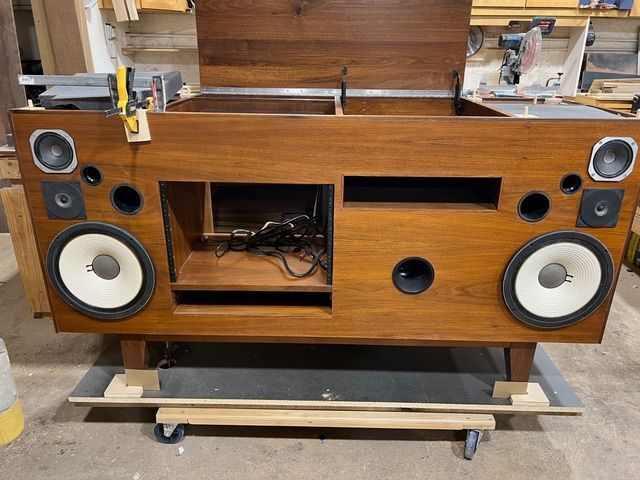 Wooden audio console with speakers, partially open. Brown wood, front-facing, visible electronics inside.