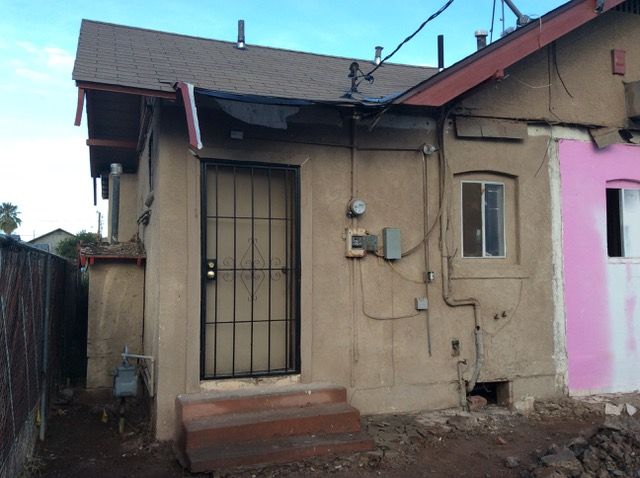 Back of a stucco building with a barred door, window, and electrical boxes.