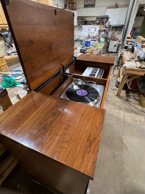 Wooden record player cabinet with open top, turntable, and other storage in a workshop.