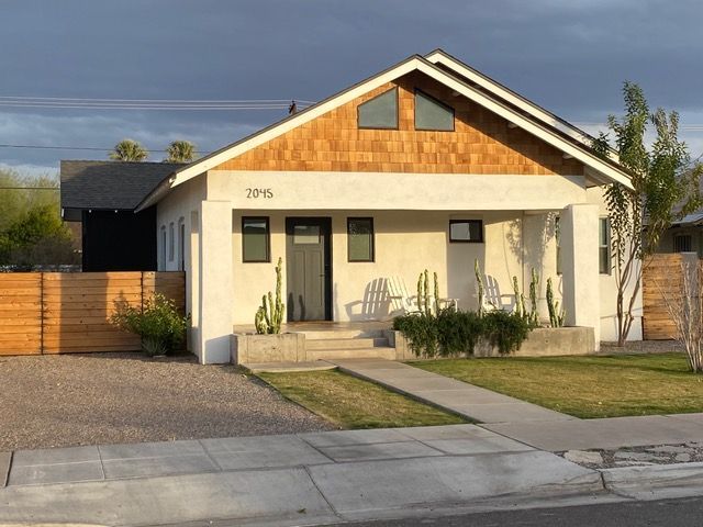 White bungalow with cedar shingle gable, front porch, cacti, and wooden fence.