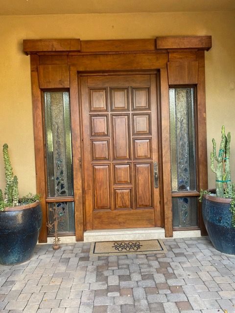 Wooden door with sidelights, set in a light-colored wall. Two cacti in blue pots flank the entry.