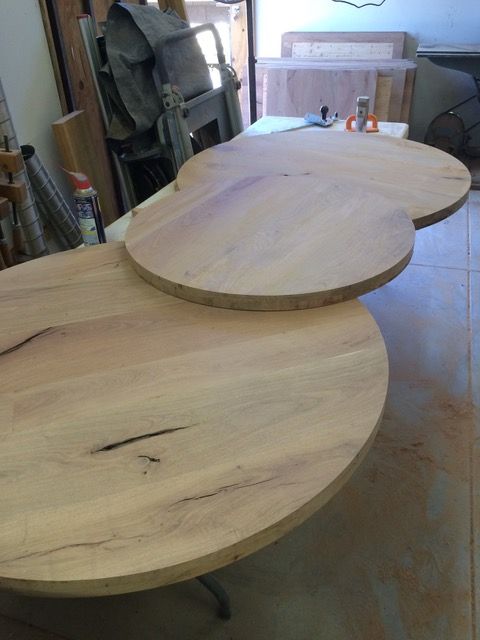 Two unfinished wooden tabletops, one slightly overlapping the other in a workshop setting.