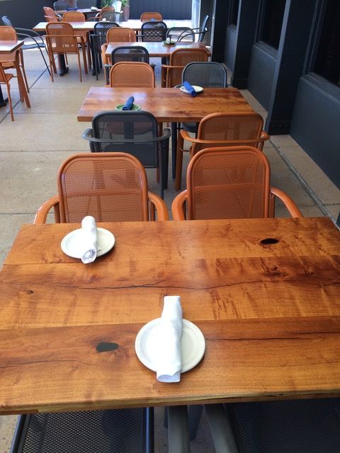 Outdoor restaurant seating; wooden tables with chairs, set for dining.