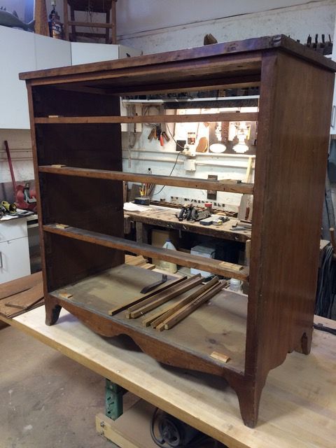 Wooden bookshelf undergoing restoration in a workshop. Shelves and trim pieces are removed.