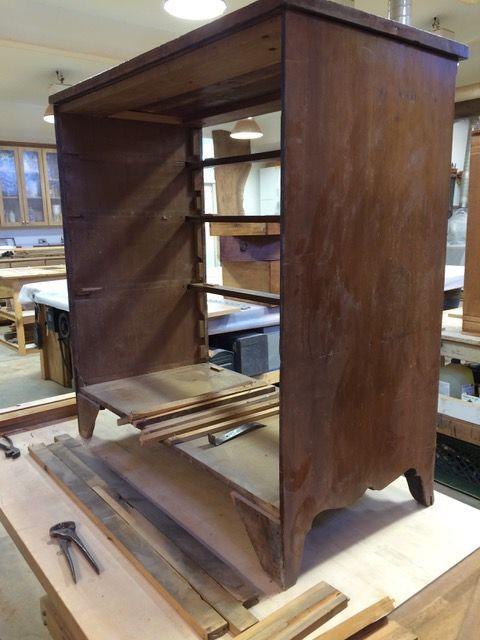 Brown wooden cabinet with open shelves, sitting on a workbench in a workshop.