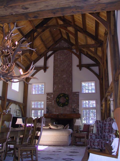 Spacious living room with exposed wooden beams, brick fireplace, and antler chandelier.