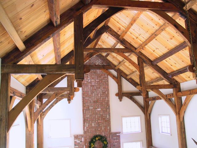 Rustic wooden beams supporting a light wood ceiling above a brick fireplace and windows.