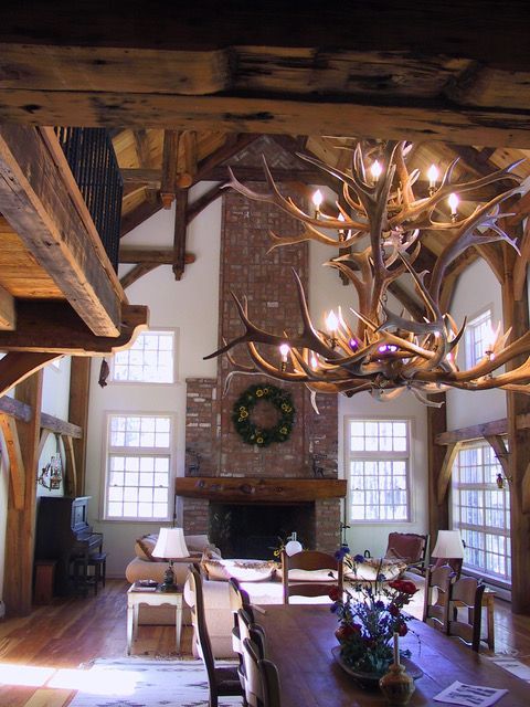 Rustic living room with antler chandelier, brick fireplace, and exposed wooden beams.