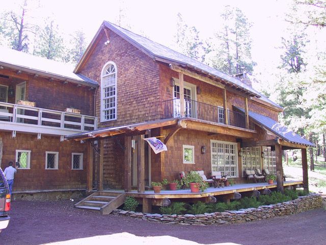 Wooden two-story house with a wrap-around porch and balcony, set in a wooded area.
