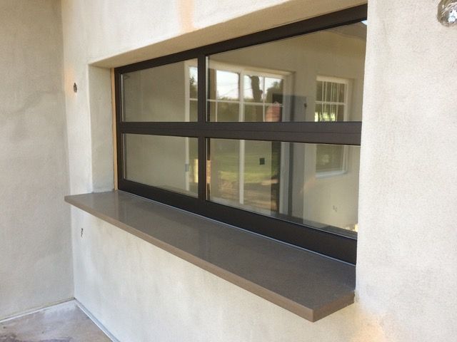 Black-framed window with a gray countertop built into a light stucco wall. A second window is reflected in the glass.