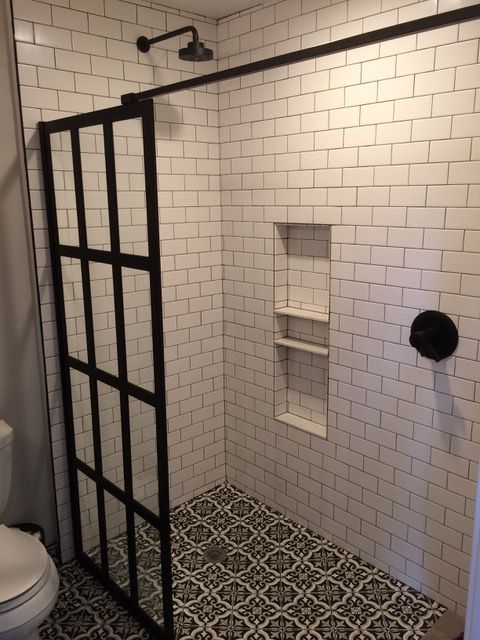 Shower with subway tile walls, black framed glass door, patterned floor, and black fixtures.