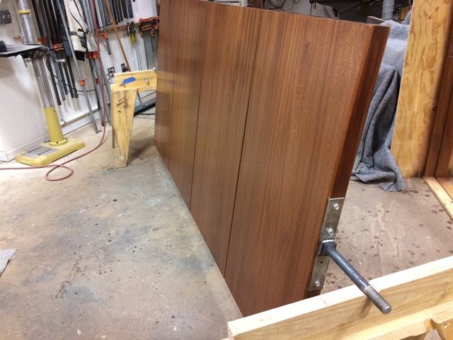 Large brown wooden door section leaning against a workbench with tools in the background.