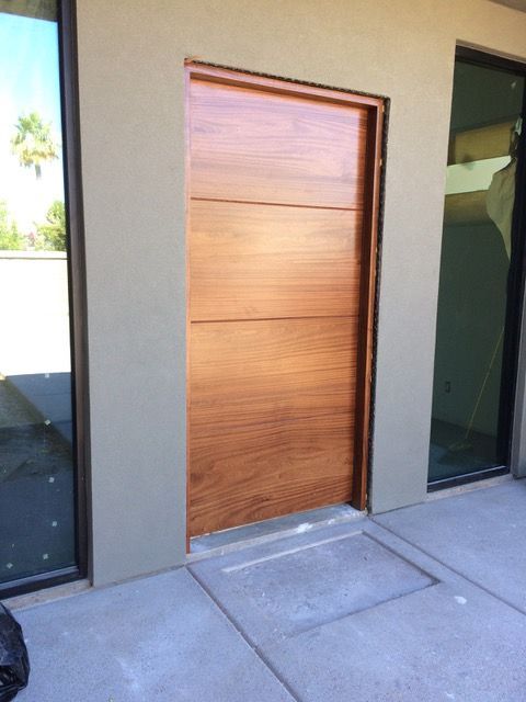 Wooden door in a recessed doorway, surrounded by gray stucco and concrete.