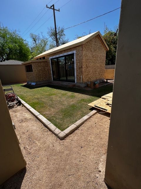Construction of a small shed with sliding glass doors; green lawn and dirt pathway surround it.