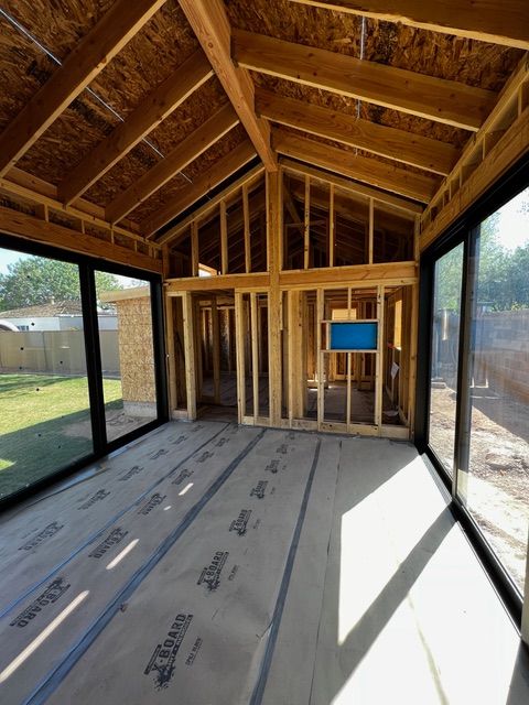 Interior of a sunroom under construction with wooden framing and large glass windows.