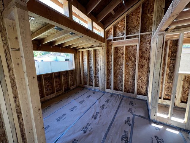Interior view of a wooden framed room under construction, with exposed beams and sheathing, and a large window.