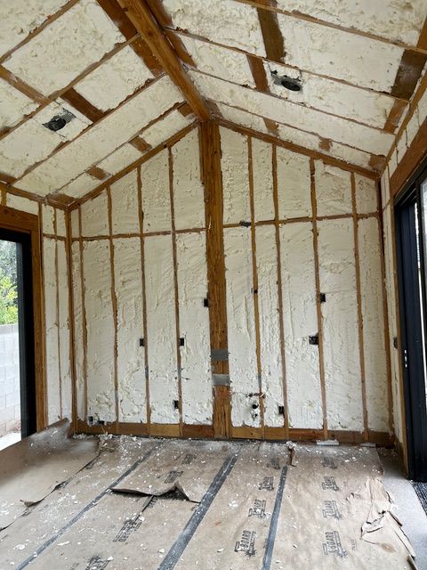 Interior of a room under construction, with exposed wooden beams and spray foam insulation.