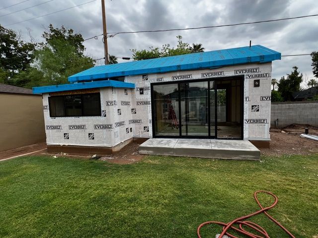 Exterior view of a small building under construction, with blue roofing and a large sliding glass door.