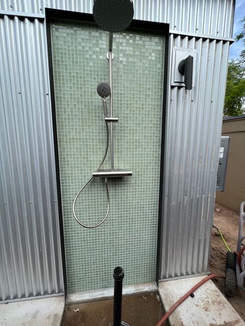 Outdoor shower with green tile backing and corrugated metal walls.