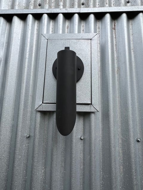 Black stove pipe on metal building wall with rectangular metal plate.