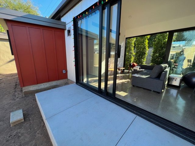 Exterior of a modern home with red shed, concrete patio, and sliding glass doors.