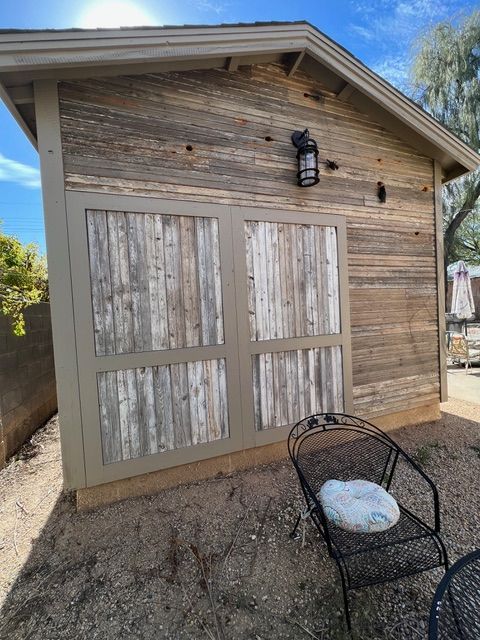 Rustic wooden shed with double doors, outdoor lamp, and a wrought iron chair.