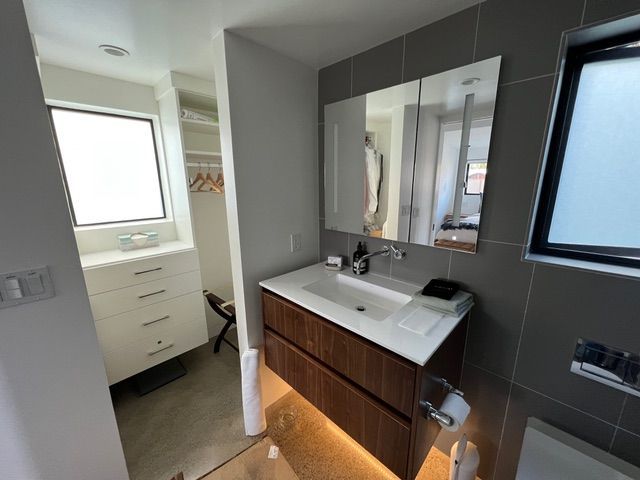 Modern bathroom with vanity and walk-in closet visible. Gray tile walls, brown vanity, and bright white closet interior.