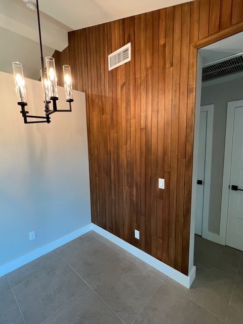 Dining room with wood accent wall, chandelier, and tan tile floor.