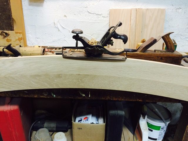 Hand plane on curved wooden plank in a workshop.