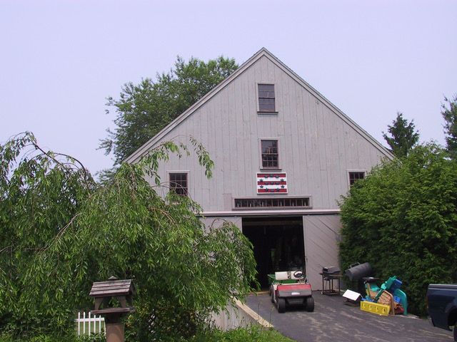 Gray barn with open door, trees, a golf cart, and a sign that is not completely readable.