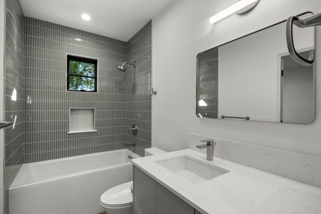 Modern gray bathroom with a tub/shower, vanity, and toilet.
