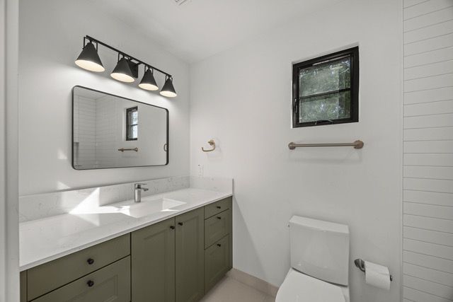 Modern bathroom with olive green cabinets, white countertop, and black-framed mirror.