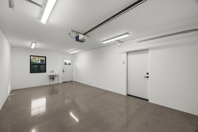 Empty garage with white walls, gray floor, overhead lights, and two doors.