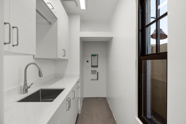 White laundry room with a sink, cabinets, a narrow doorway, and a window.