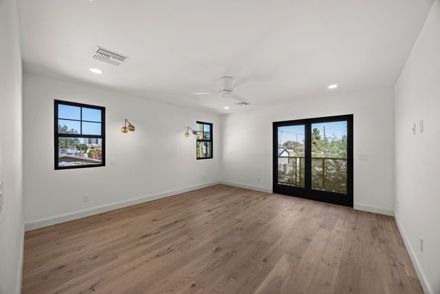 Empty room with wood floor, white walls, black-framed windows, and French doors leading to a balcony.