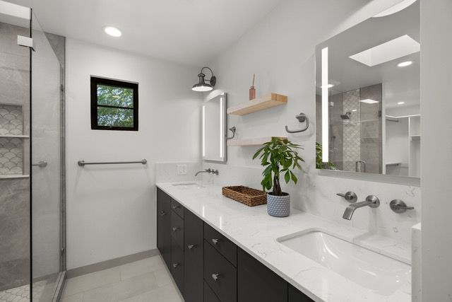 Modern bathroom with white countertops, dark cabinets, a shower, and two sinks.