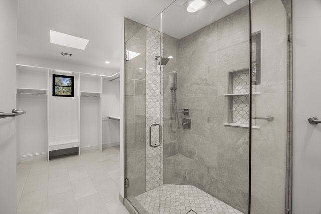 Modern bathroom with a glass shower, walk-in closet, and gray and white tiling.
