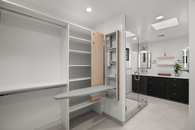 Walk-in closet with built-in ironing board, shelving, and bathroom with black vanity.