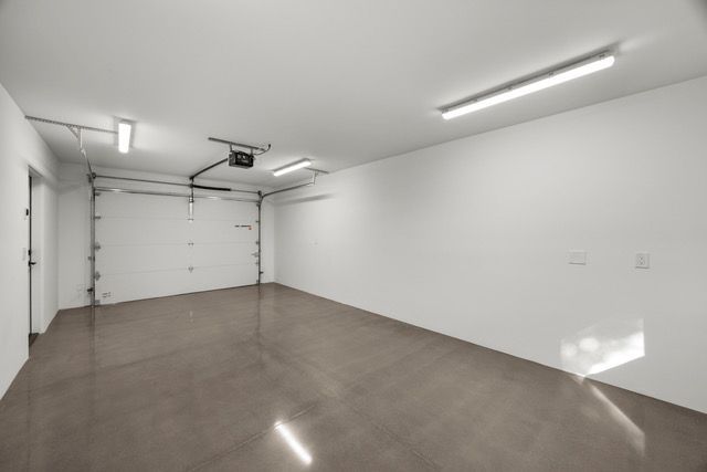 Empty, freshly painted garage; closed white door, bright lighting, gray floor.