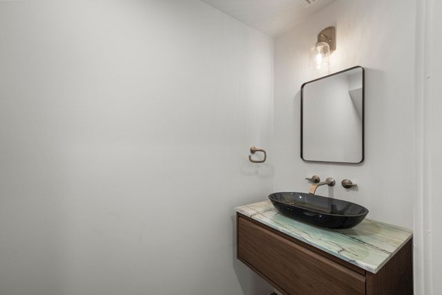 Small bathroom with floating wooden vanity, oval sink, marble countertop, and rectangular mirror.