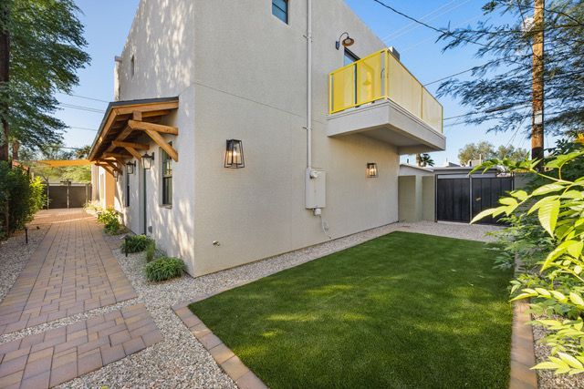 Exterior of a modern two-story house with a small backyard, pathway, and yellow balcony.
