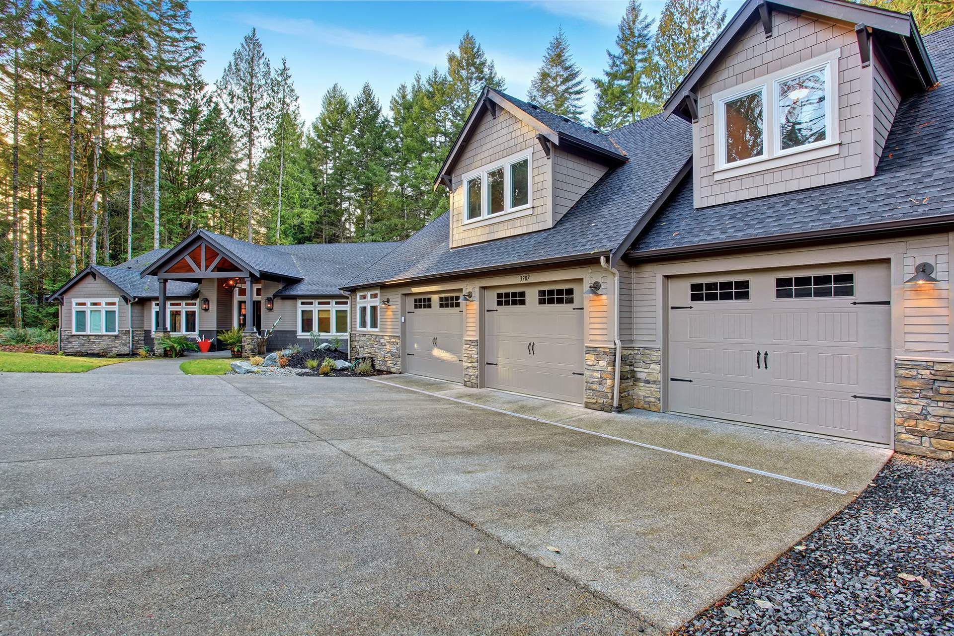 A large house with three garage doors is surrounded by trees.