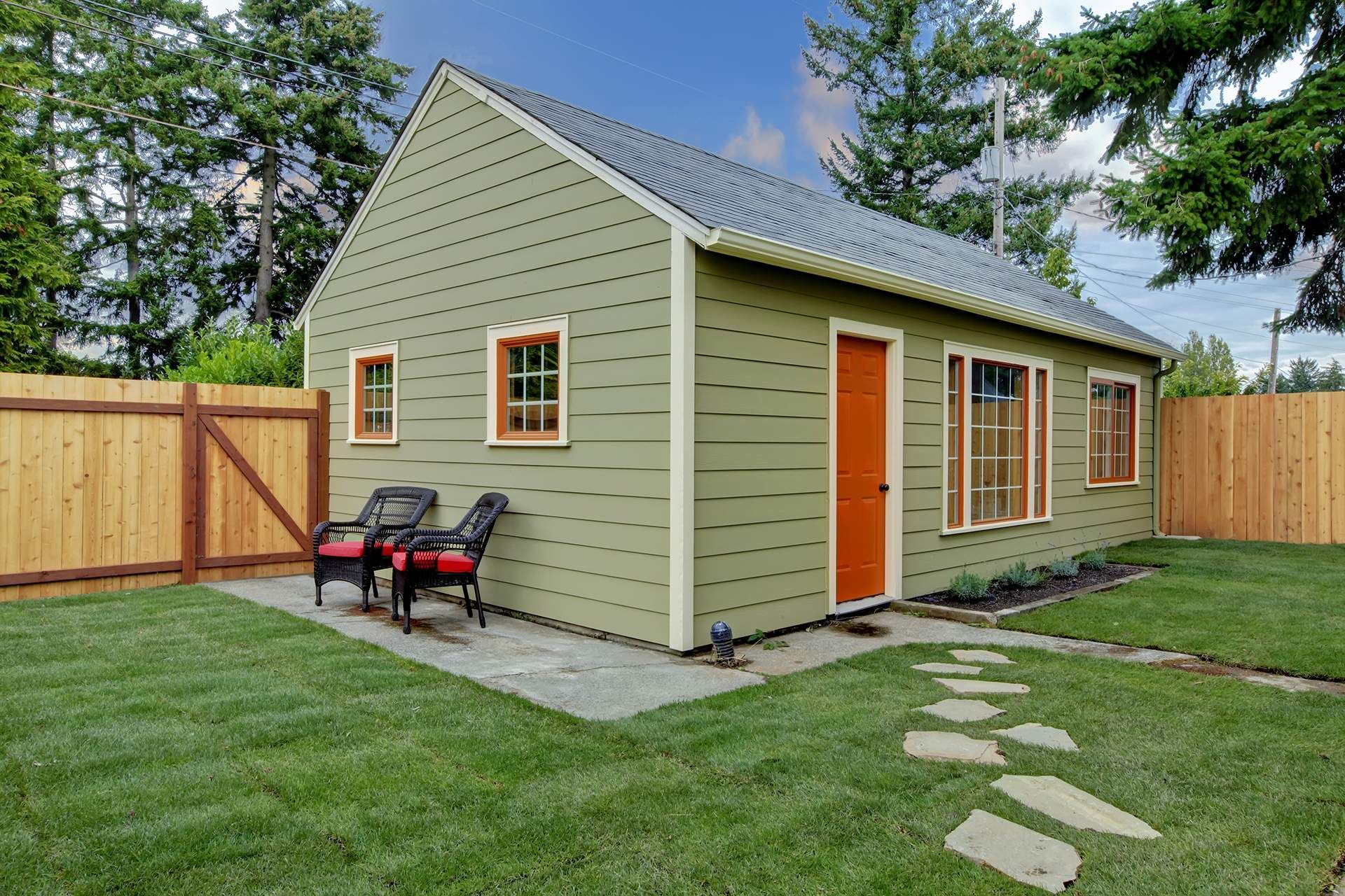 A small green house with a wooden fence in the backyard.