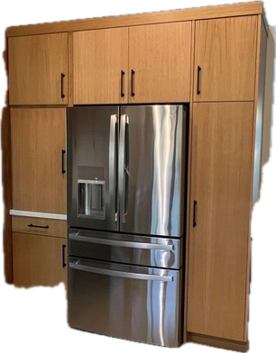 Refrigerator surrounded by light wood cabinets with black handles.