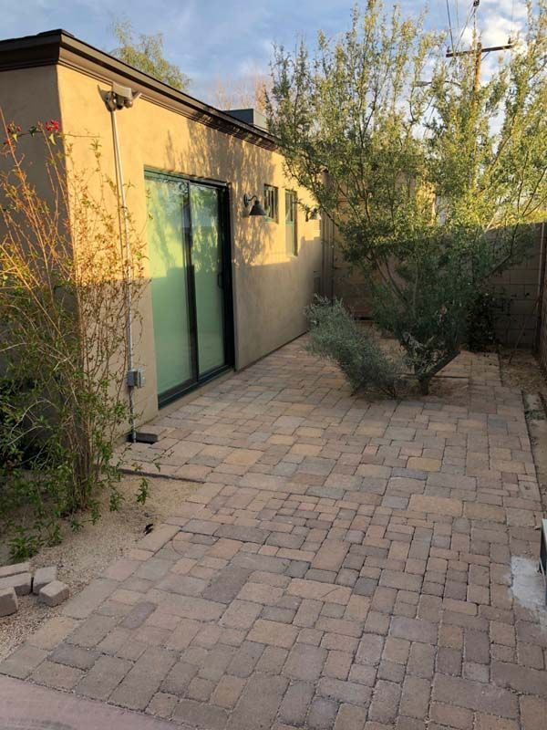 Patio paved with bricks, next to a tan building with a sliding glass door and desert landscaping.