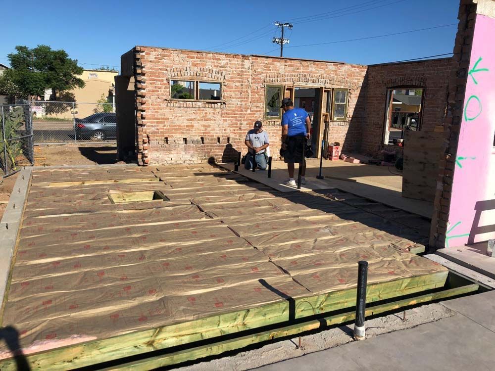 Two men are standing in front of a brick building under construction.