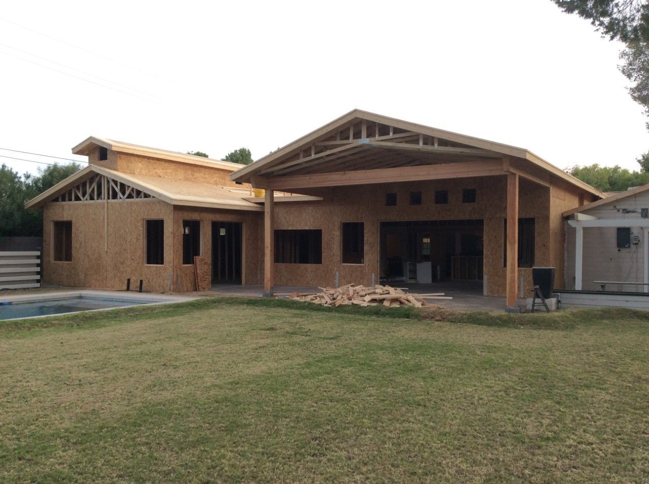 House under construction with exposed wooden frame and patio overlooking a lawn and pool.