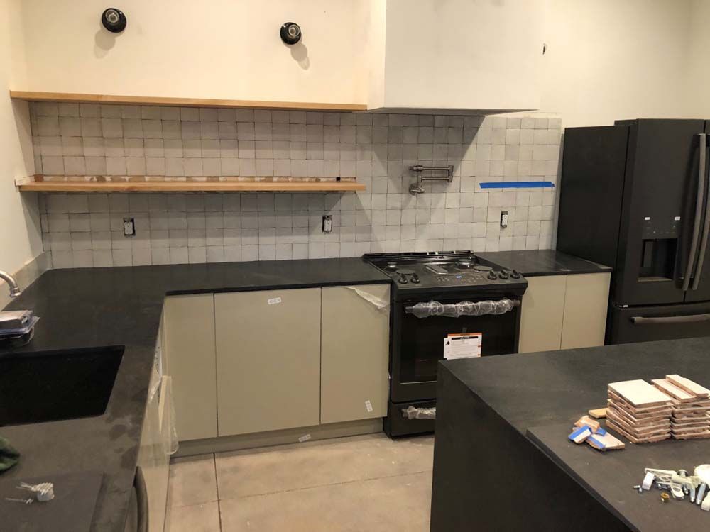 A kitchen with a stove , refrigerator , sink , and shelves.