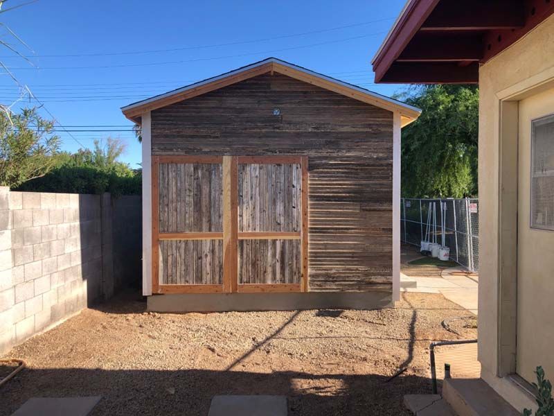 A small wooden building with a roof is in the backyard of a house.