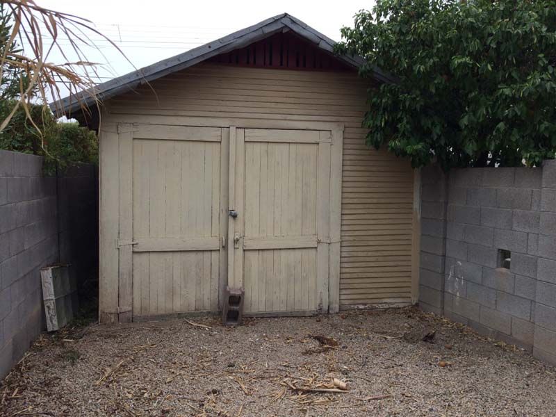 A small wooden garage with a brick wall and a tree in the background.